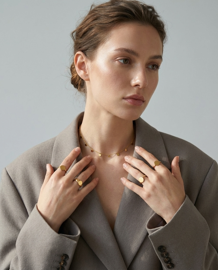 Woman wearing the gold disc charm necklace styled with a blazer, showing the elegant layered jewellery look.