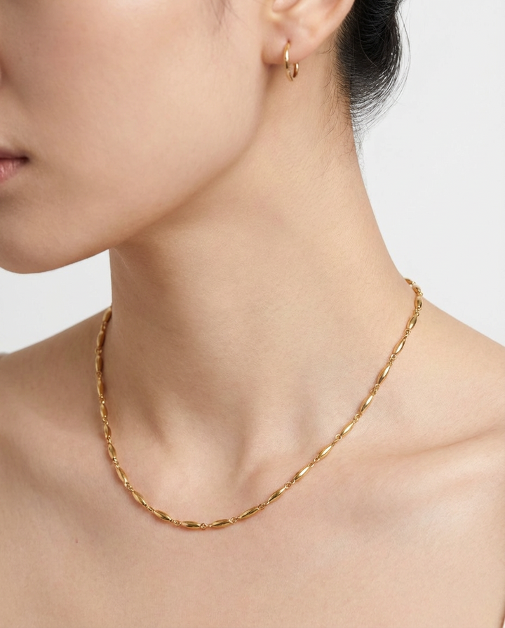 Close-up of the gold oval link chain necklace on the neckline, highlighting the polished oval links.