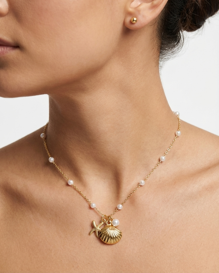 Close-up of the gold seashell and starfish pendant necklace on the neckline, showing the detailed pendant design.