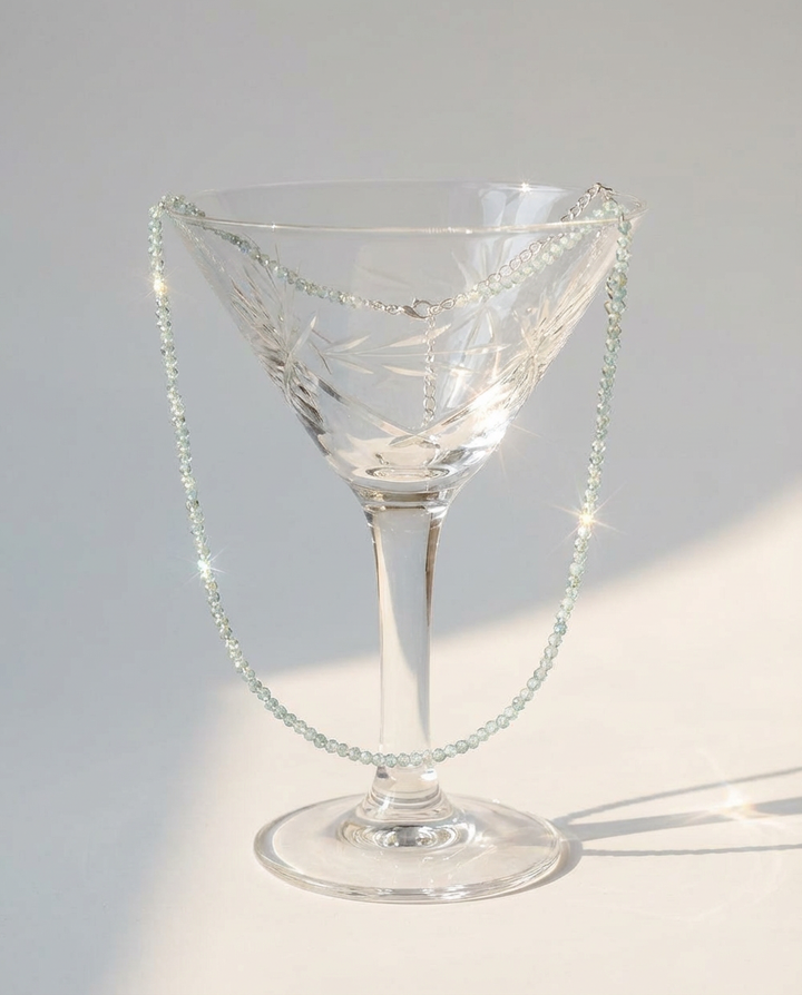 The light blue beaded necklace draped over a glass, styled in an elegant minimal decorative setup.
