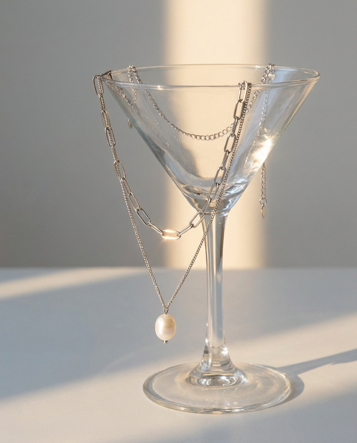 The silver chain and pearl pendant necklace displayed over a glass, styled in an elegant decorative setup.